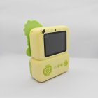 Green kids print camera with Dinosaur decorative attachment, integrated rear screen and easy-control buttons, compliant with safety standards.