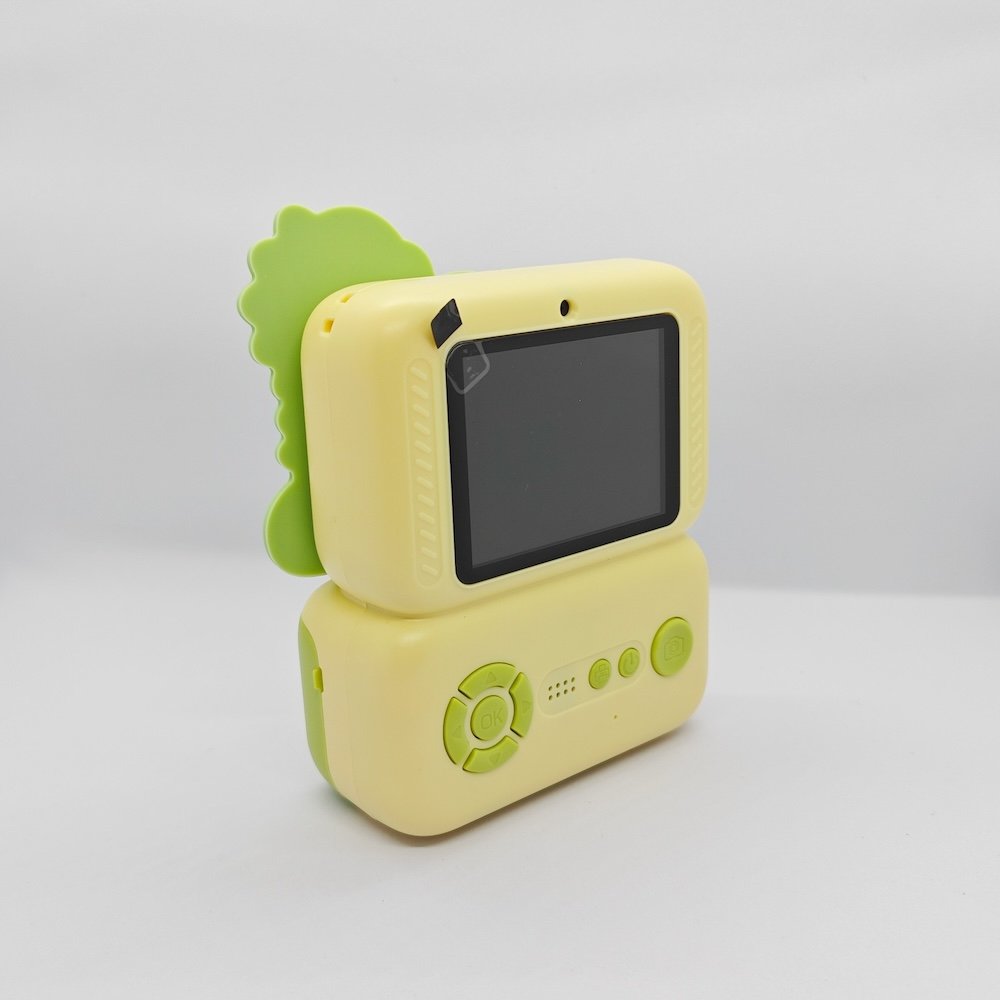 Green kids print camera with Dinosaur decorative attachment, integrated rear screen and easy-control buttons, compliant with safety standards.